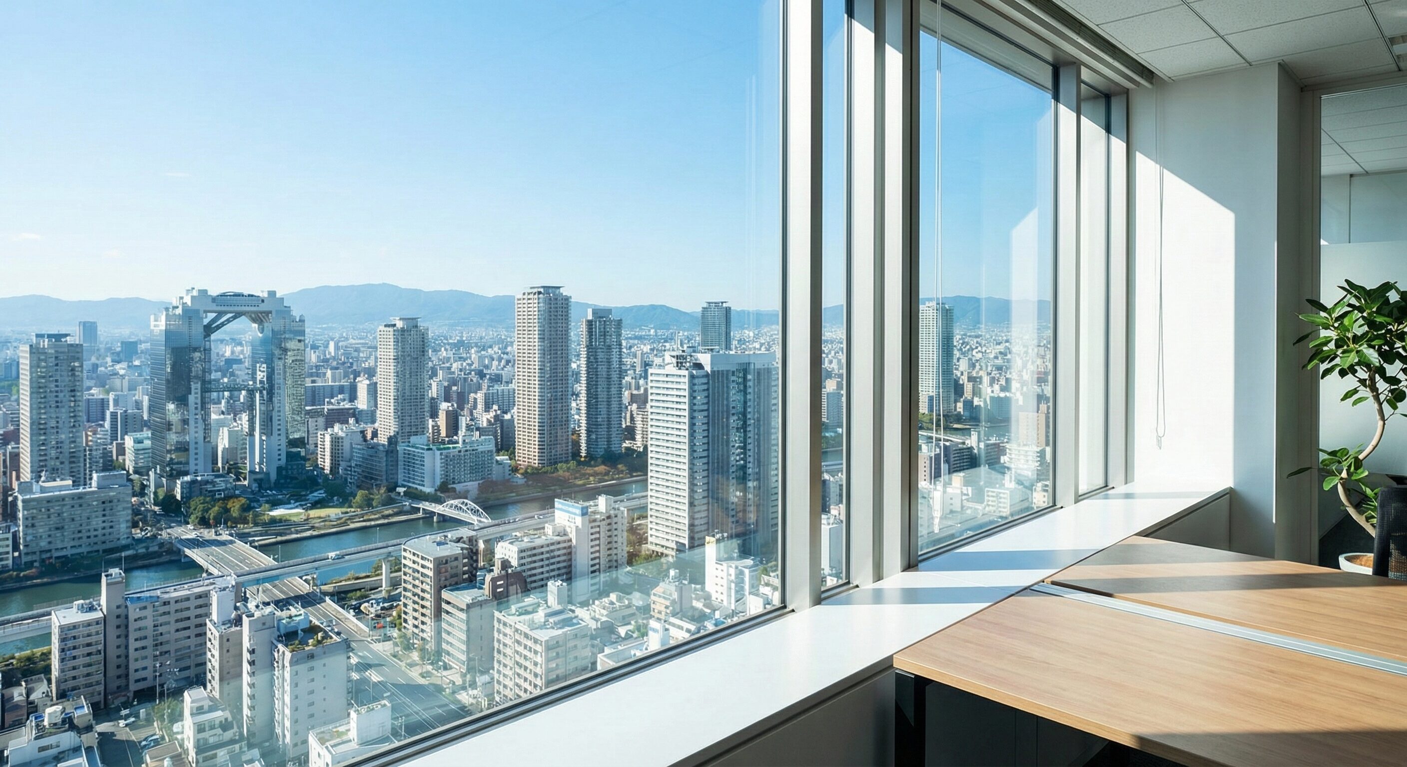 高層ビルの窓から見下ろす大阪の都市風景。晴天の空と広がるビジネス街が、将来への展望と成長の可能性を象徴する構図。